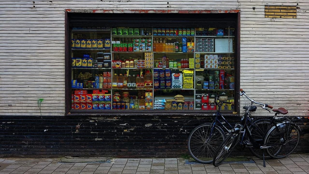 Storefront of a small grocery store with stocked shelves and a bicycle outside