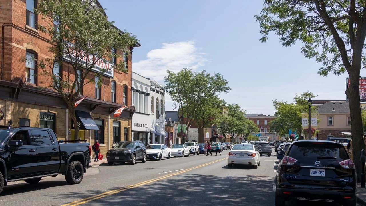 Looking south along Brock Street in downtown Whitby, Ontario, on a sunny summer day; storefronts, traffic lights and parked cars, no identifiable people.
