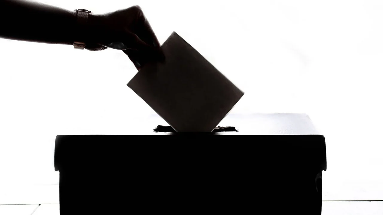 Silhouette of a hand placing a ballot into a ballot box.