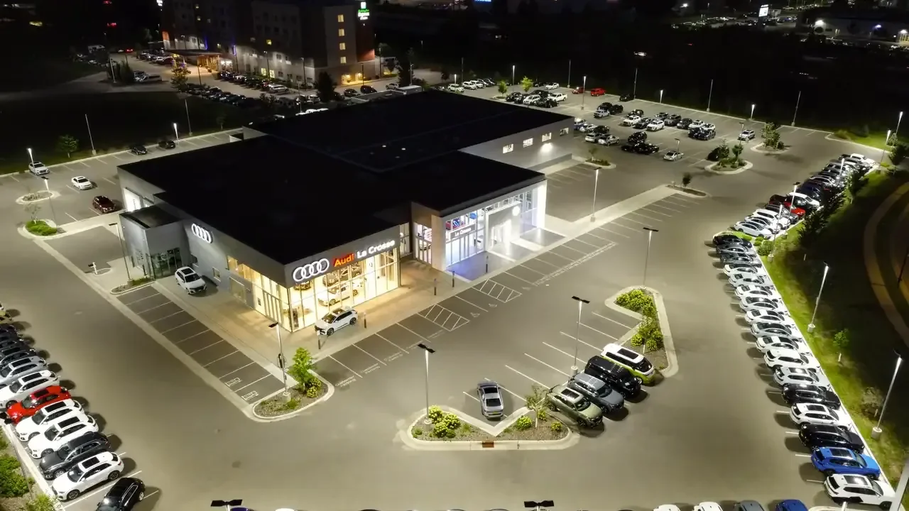 Aerial night view of a car dealership showroom surrounded by rows of parked vehicles
