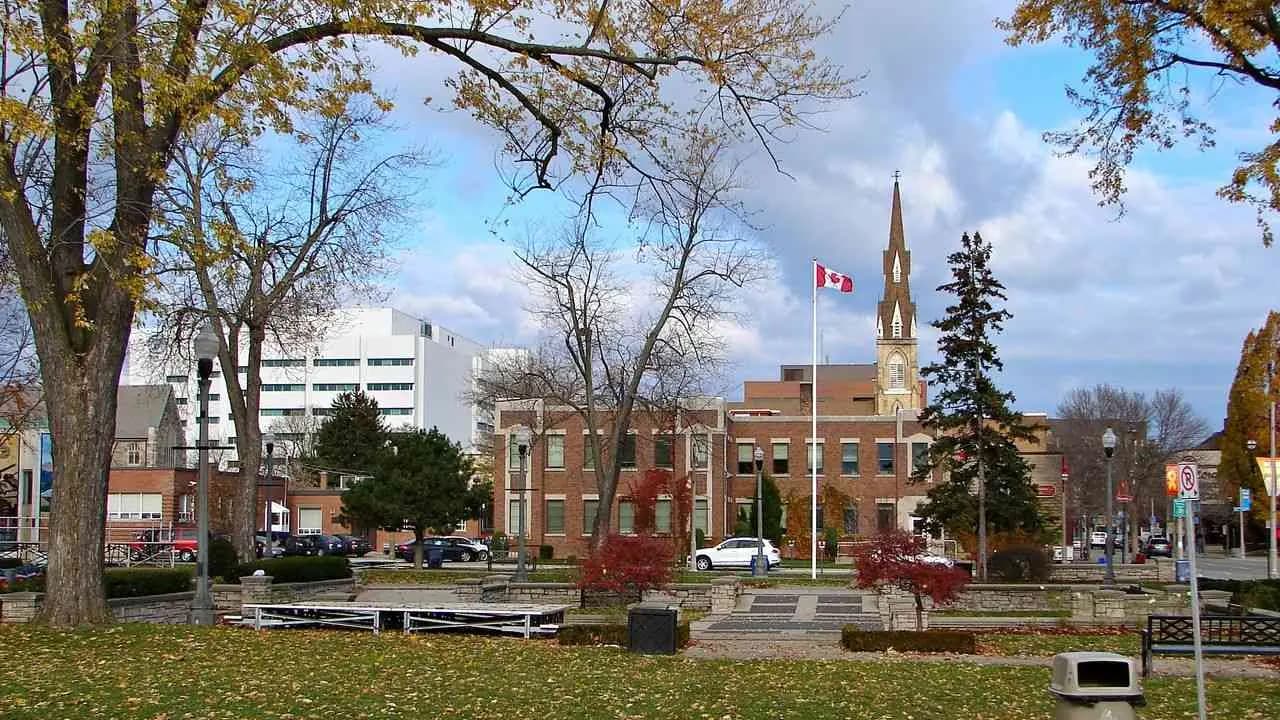 A park and civic buildings in downtown Oshawa, Ontario, with a Canadian flag and a church spire; no people visible.