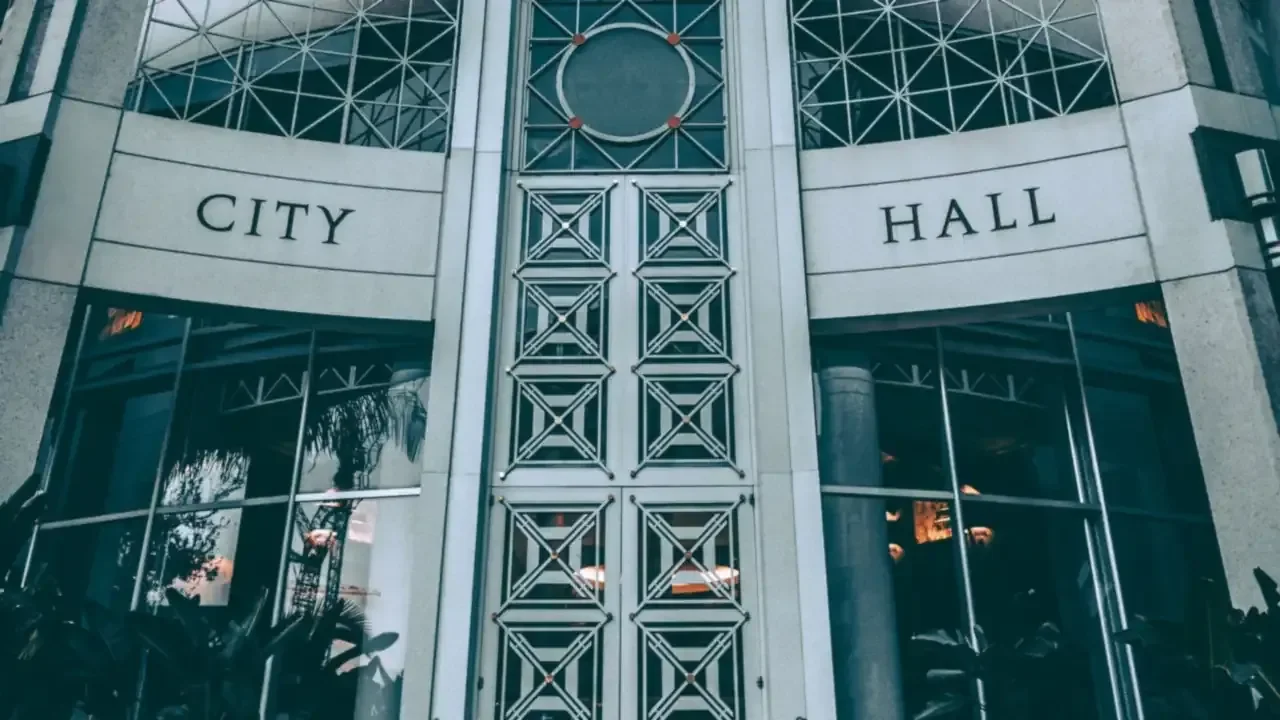 Entrance of a modern city hall building with 'CITY HALL' lettering above the glass doors